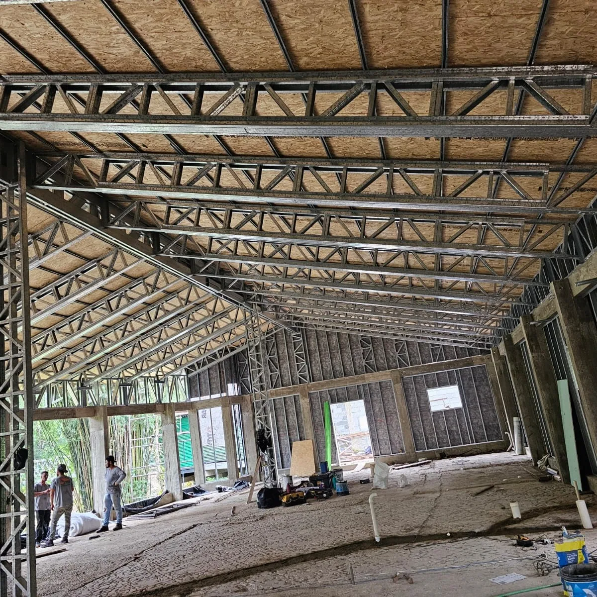 Interior de um salão com a cobertura em treliças de aço e placas de OSB vista de baixo.