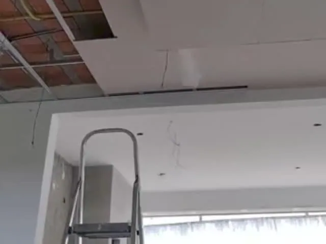 Forro em placas de drywall numa sala em obra, com a estrutura de perfis aparecendo numa abertura e uma escada à frente.