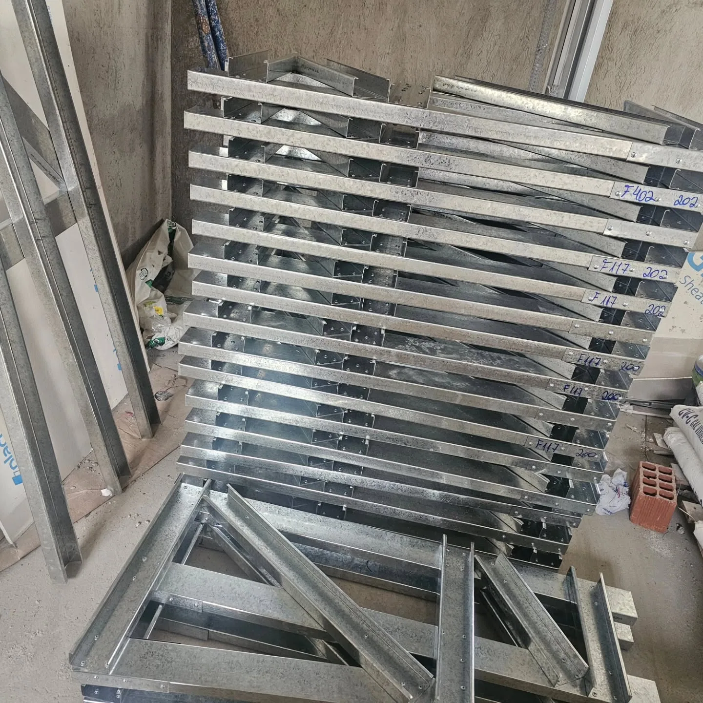 Perfis de aço galvanizado empilhados e uma treliça sobre o chão da obra.
