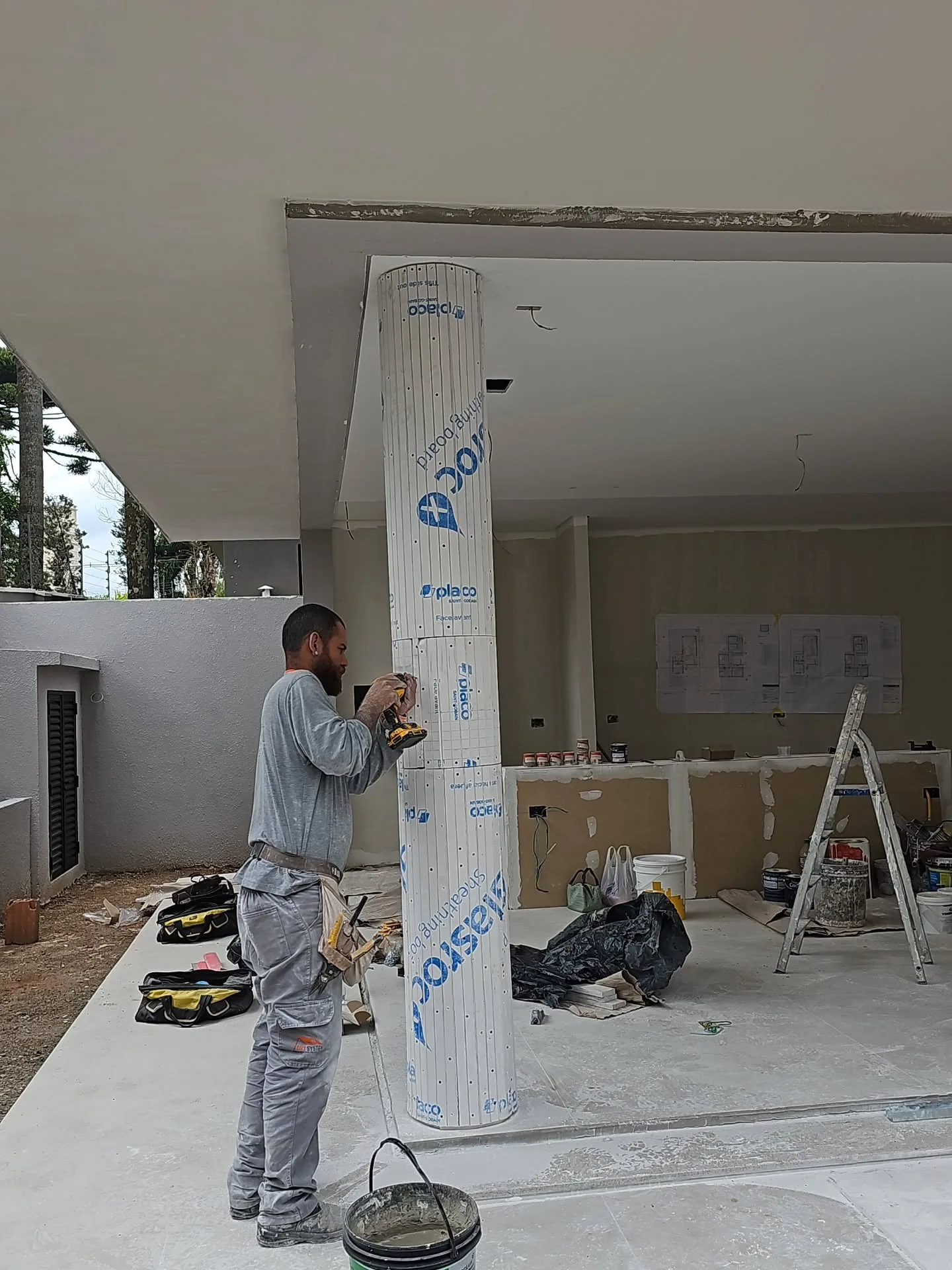 Funcionário parafusando placas Glasroc que envolvem o pilar do salão.